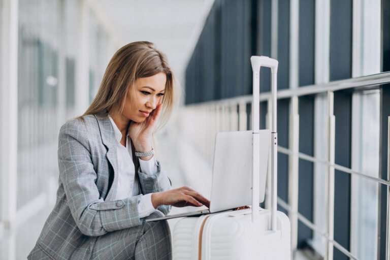 Young woman with travel bag, booking a flight on laptop in airport